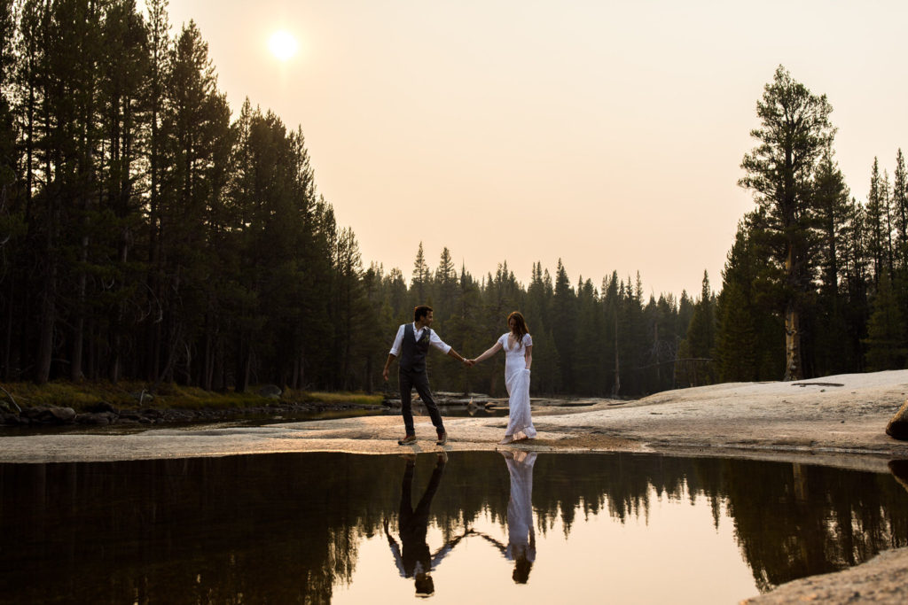 Couple holding hands with their reflections in a still forest lake