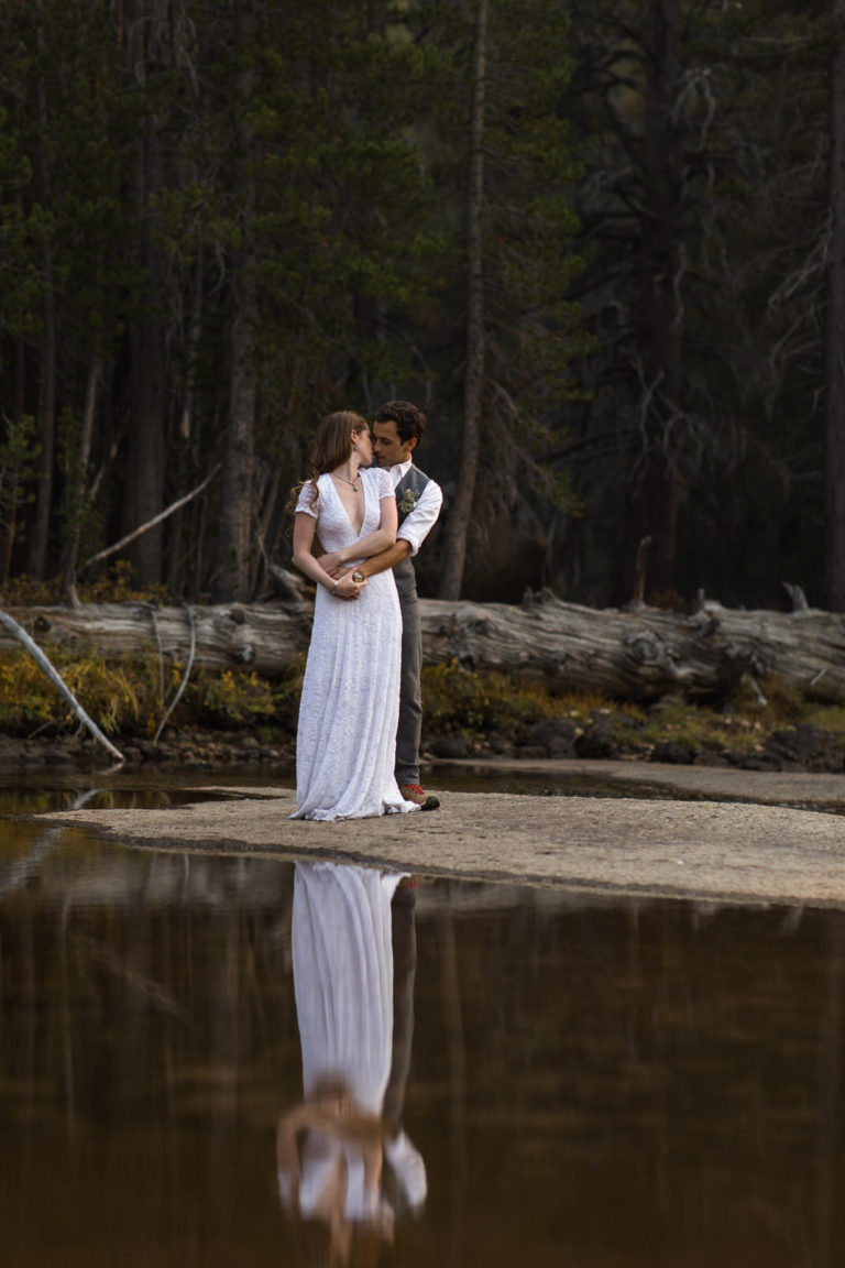 Couple embracing at the edge of a forest pond with their reflection below