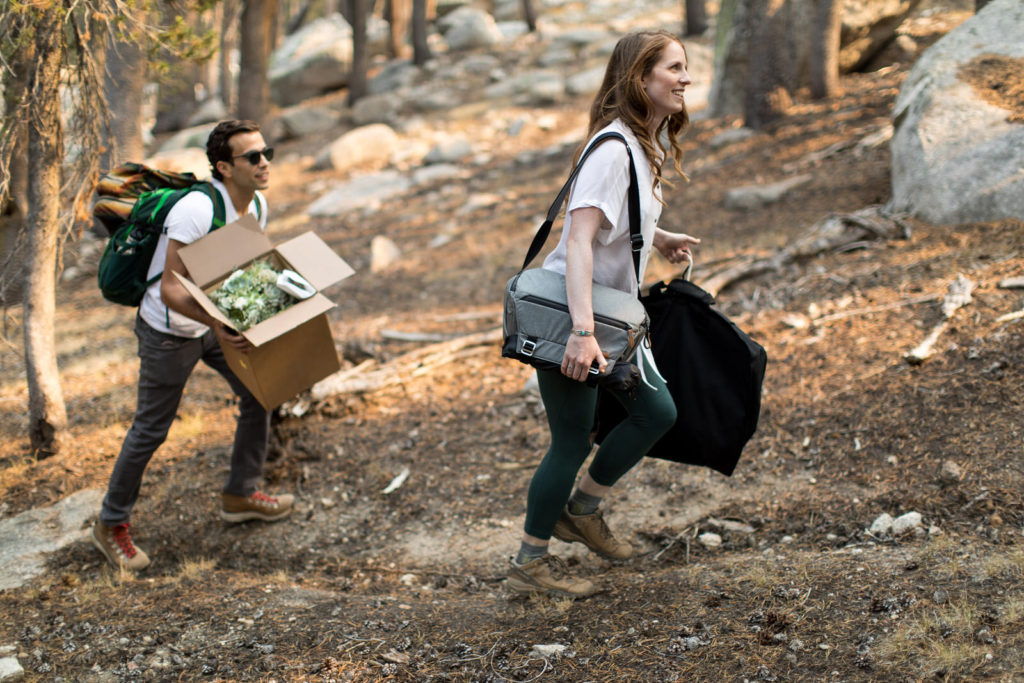 Couple carrying their wedding clothes and supplies along a forest trail