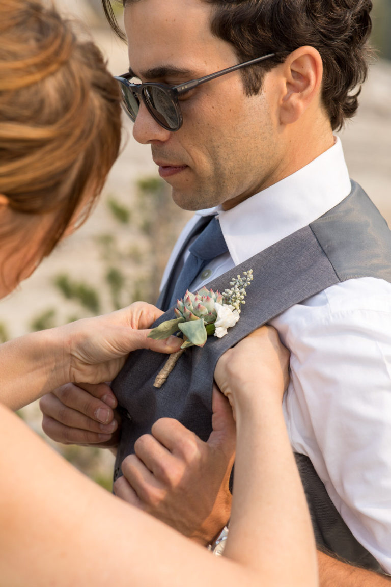 Bride pinning a boutonniere to the groom’s vest