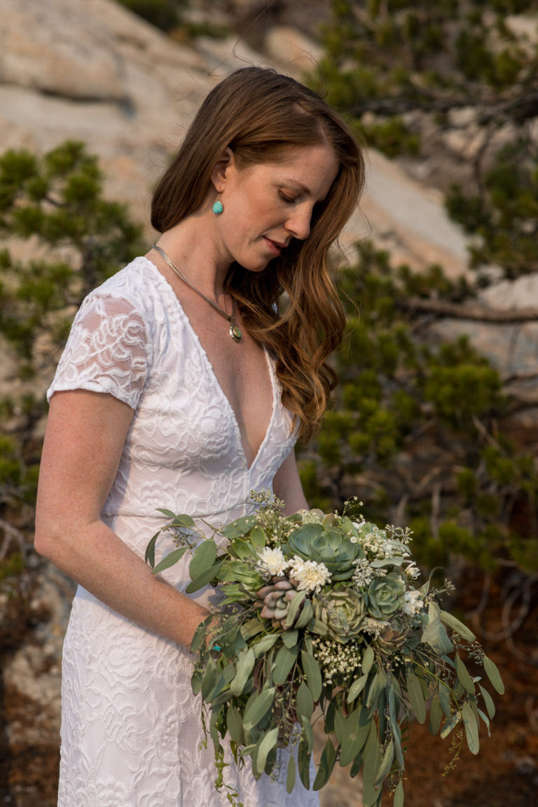 Bride holding a leafy bouquet beside granite rocks