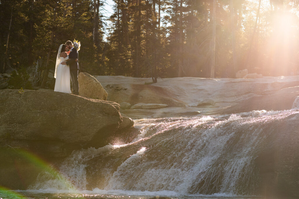 Couple embracing on a boulder beside a forest waterfall