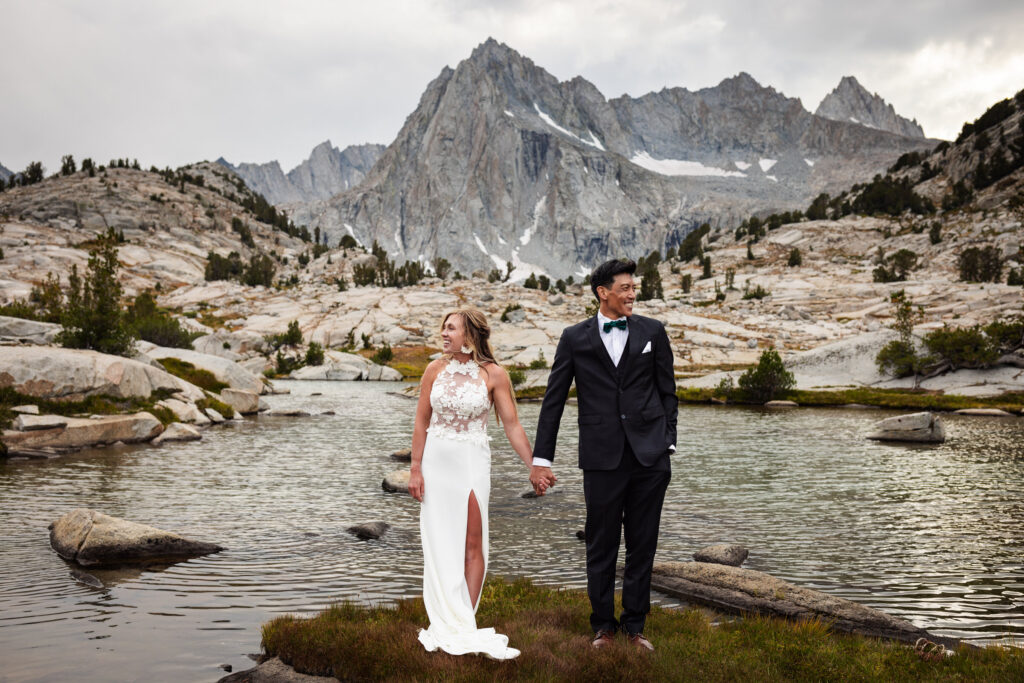 Newlyweds holding hands at the edge of a mountain lake