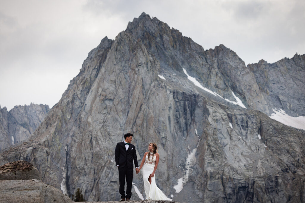 Bride and groom standing on granite beneath a jagged mountain peak