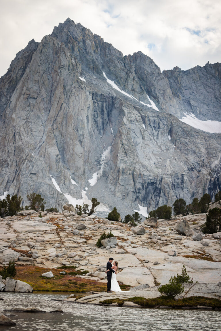Wedding couple beneath a massive granite peak across an alpine lake