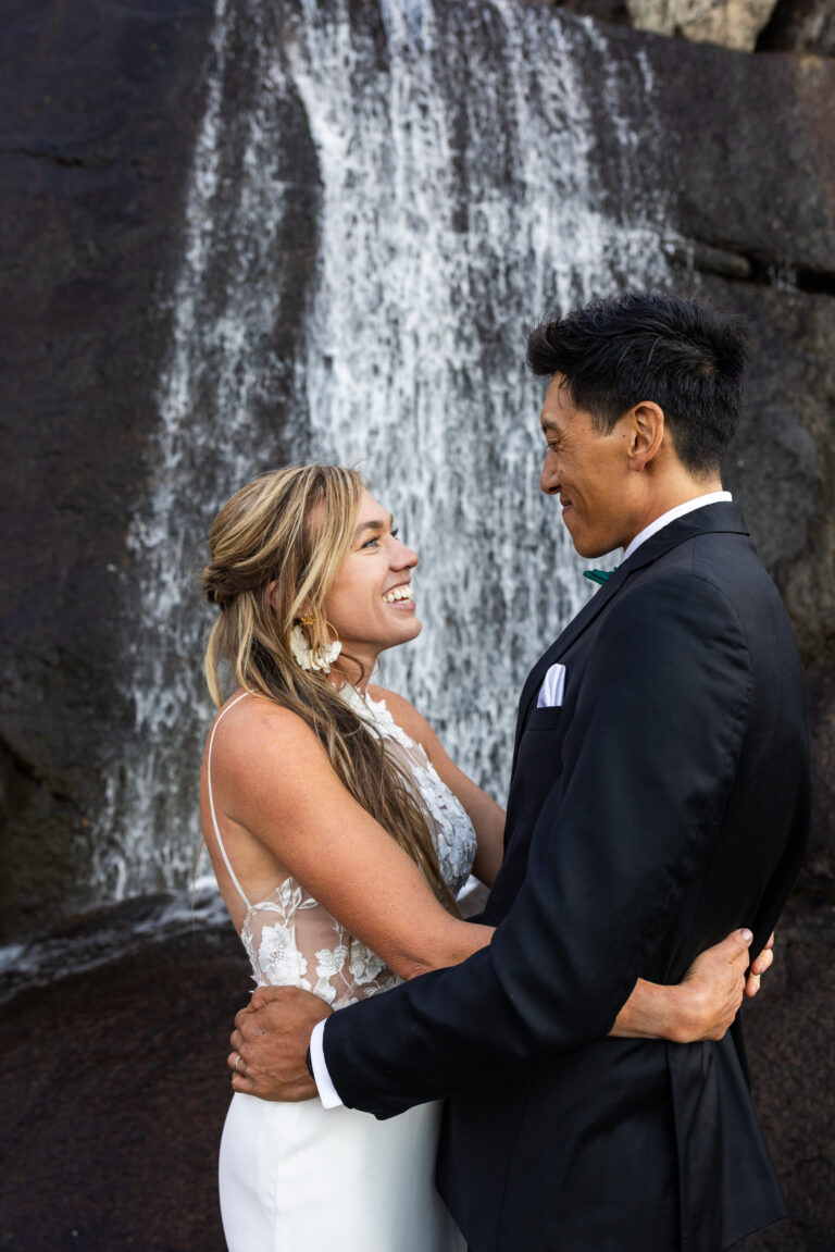 Bride and groom smiling at each other in front of a waterfall