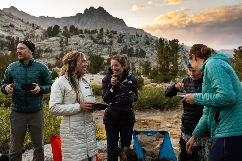 Wedding group sharing a meal outdoors beneath mountain peaks