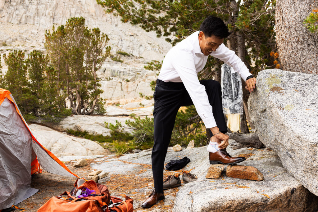 Groom putting on his dress shoes beside a tent at camp