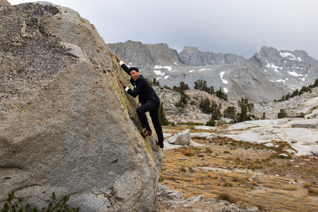 Groom climbing a granite boulder in his wedding suit