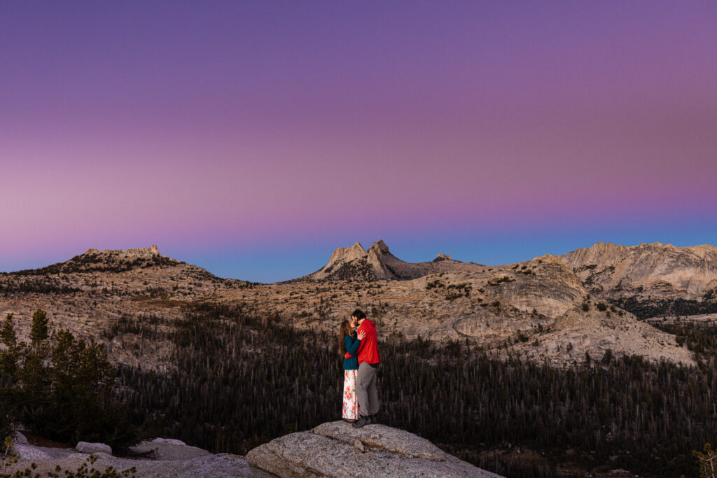 Couple embracing on a granite ridge beneath a purple twilight sky