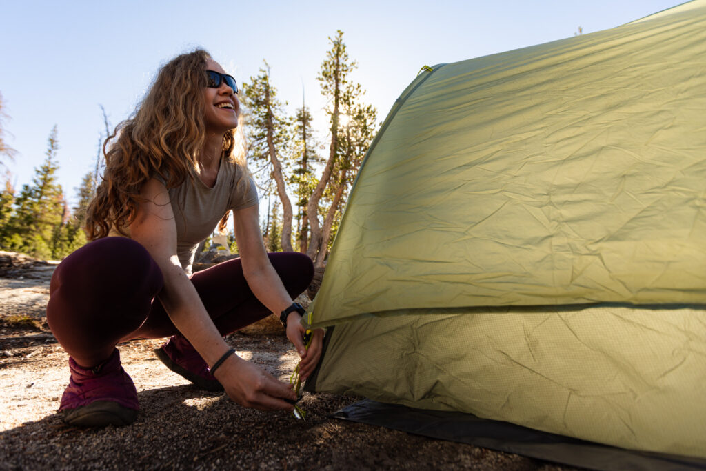 Woman setting up a green tent at a forest campsite