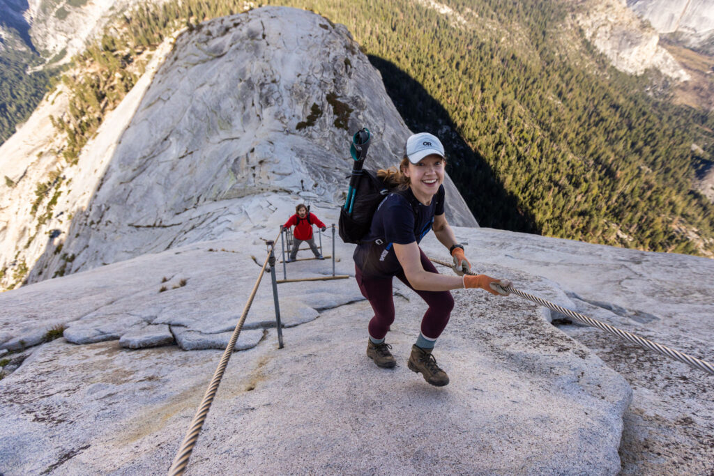Hiker ascending a steep granite slope using fixed cables