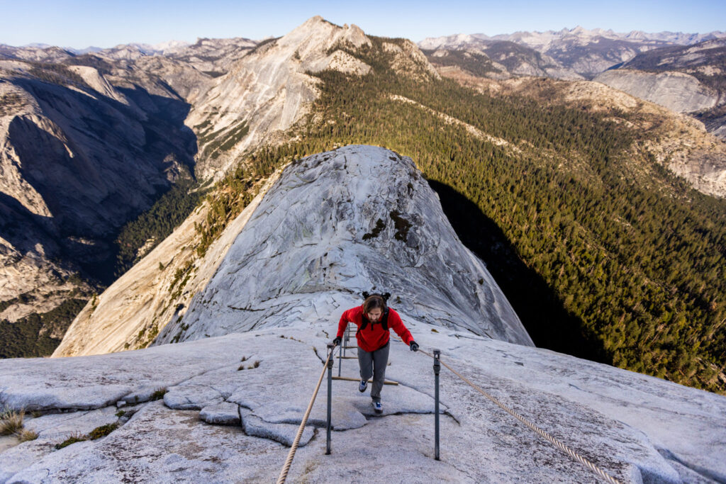 Hiker climbing fixed cables high above a mountain valley