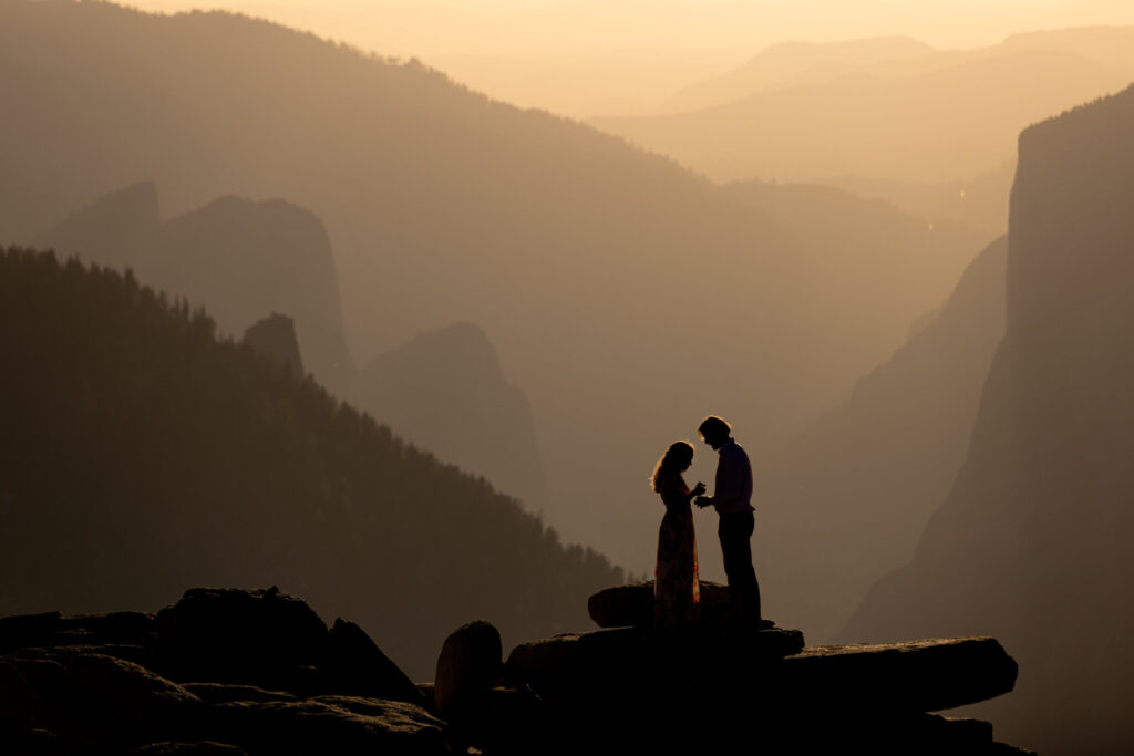 Couple silhouetted against a hazy golden valley at sunset