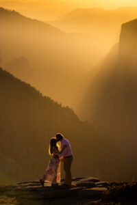 Couple embracing on a rocky ledge above a golden mountain valley
