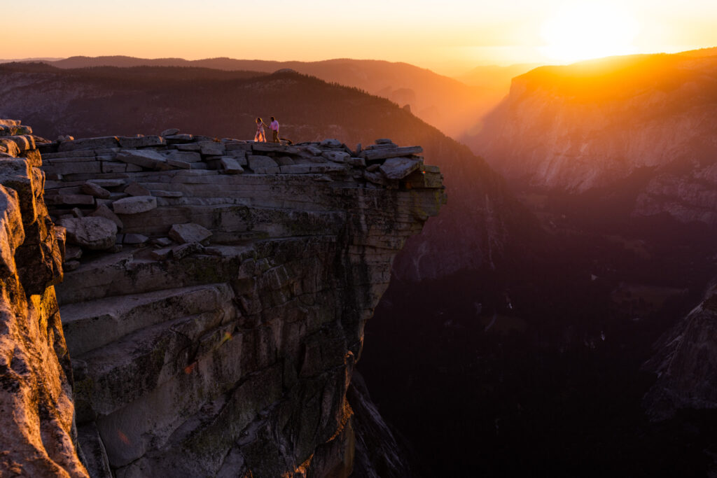 Wide view of a couple on a sheer granite cliff at sunset