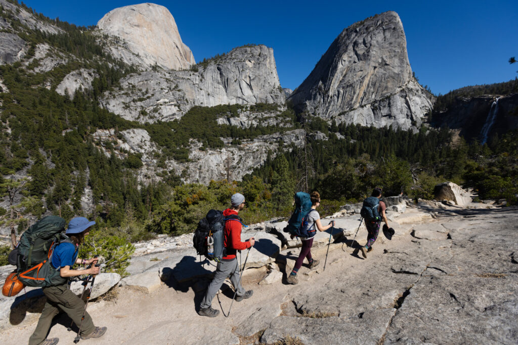Group of backpackers hiking across granite beneath mountain domes