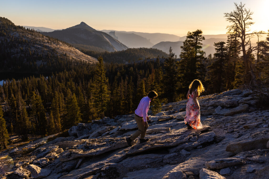 Couple walking across sunlit granite above a forested mountain valley