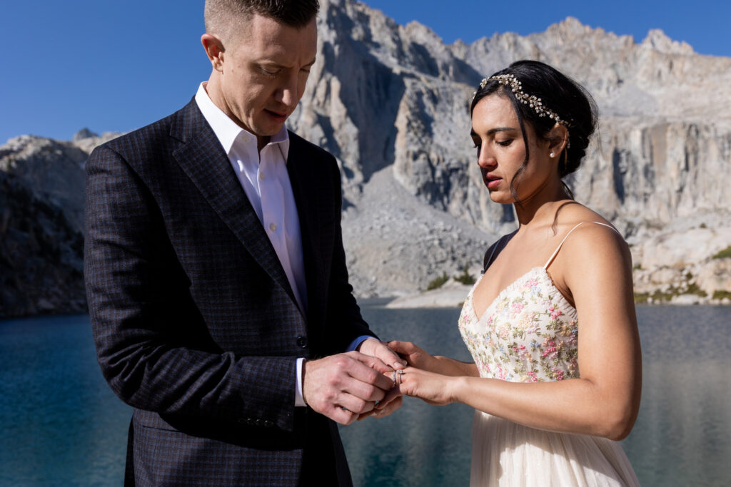 Groom placing a wedding ring on the bride’s finger beside the lake