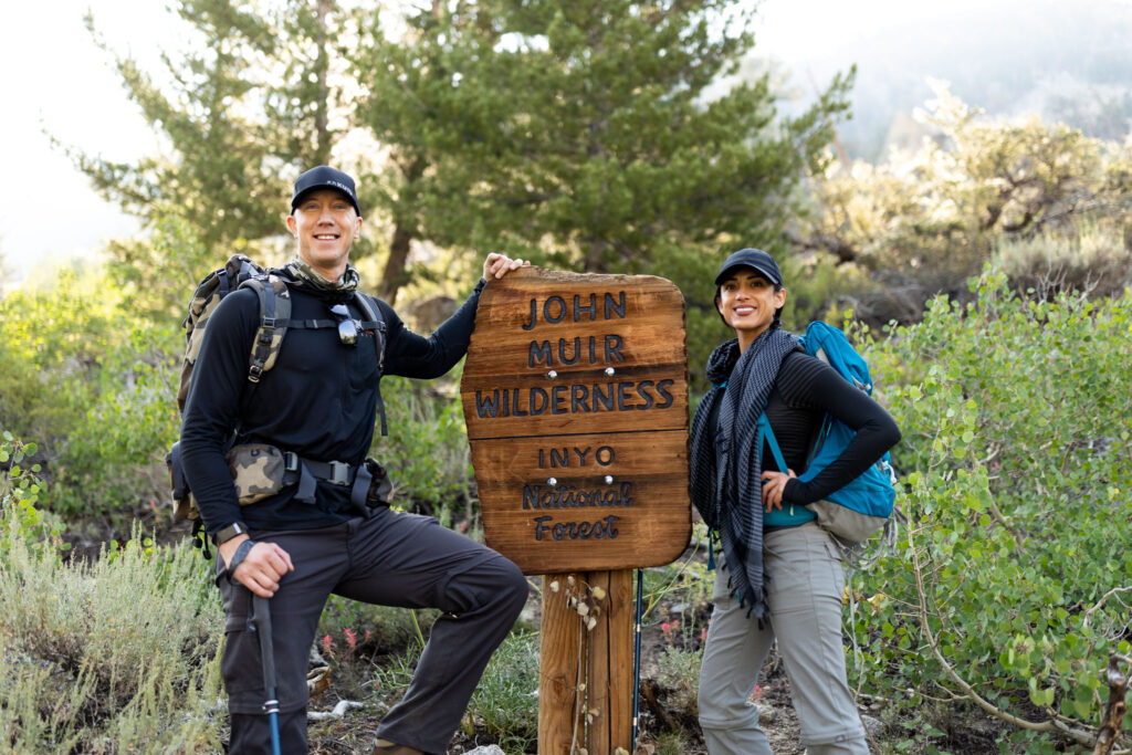 Two backpackers posing beside the John Muir Wilderness trail sign