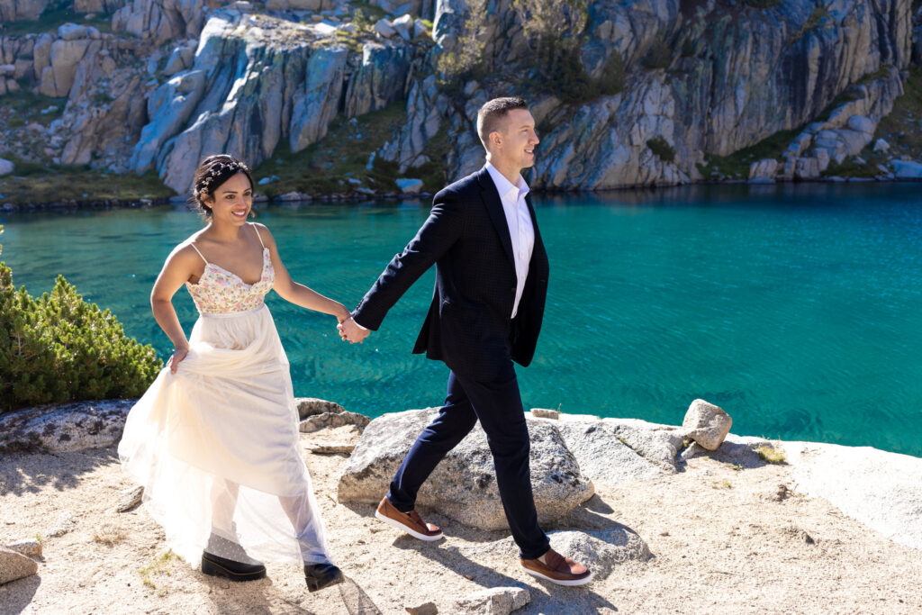 Newlyweds walking hand in hand beside an alpine lake