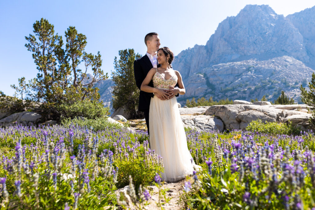 Wedding couple standing among purple wildflowers in the mountains