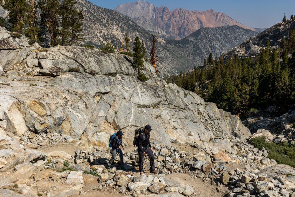Backpackers ascending a rocky trail below granite peaks