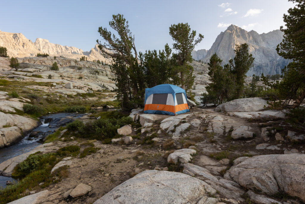 Camping tent pitched beside an alpine stream below mountain peaks