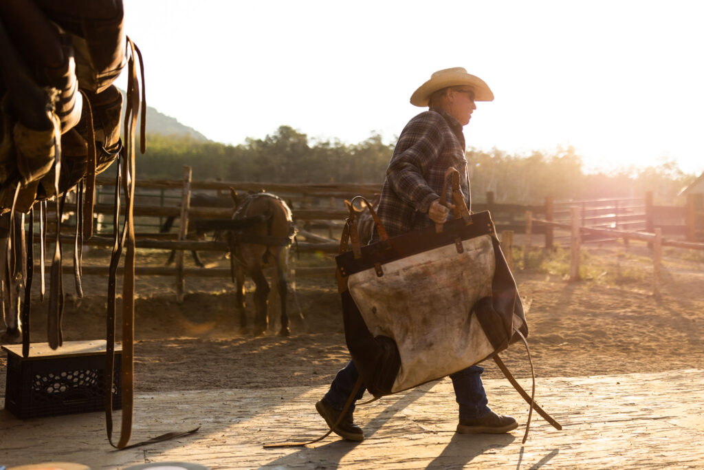 Packer carrying equipment beside a corral at sunrise